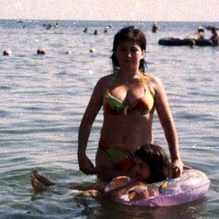 Woman stands in water, holding a child on a float.
