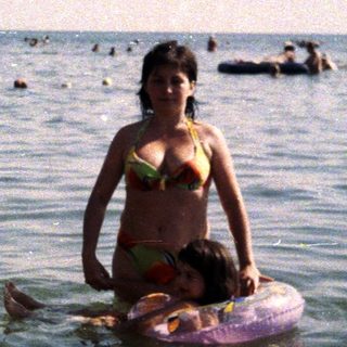 Woman stands in water, holding a child on a float.