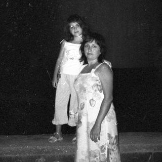 Woman and child stand outside at night, illuminated.