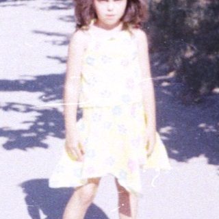 Girl stands on a street with trees and buildings.