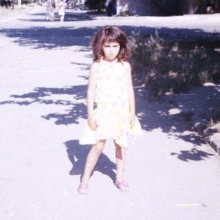 Girl stands on a street with trees and buildings.
