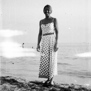 Woman in a dress stands on a beach.
