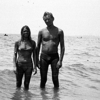 Couple stands in shallow water, facing the camera.