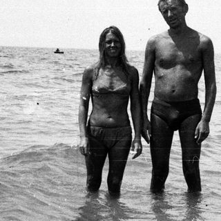 Couple stands in shallow water, facing the camera.