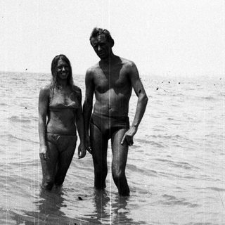 Couple standing in shallow water, appearing to be at a beach.