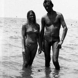 Couple standing in shallow water, appearing to be at a beach.