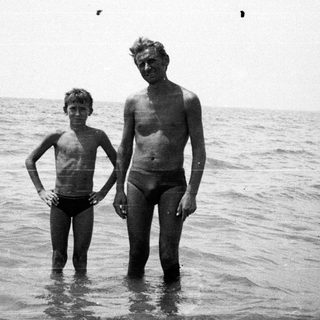 Man and boy standing in shallow water by the sea.