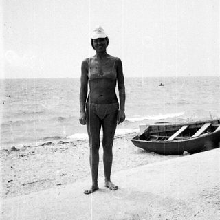 Woman stands on a beach near a small boat.