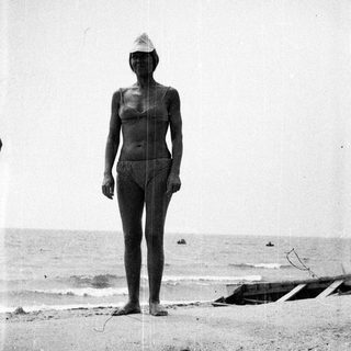 Woman in swimwear stands on a sandy beach.