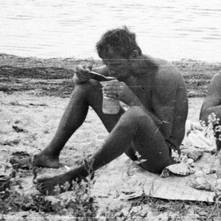 Two men seated on a blanket near a body of water.