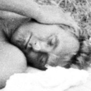 Person sunbathing on a blanket outdoors, with belongings nearby.