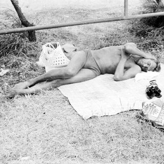 Person sunbathing on a blanket outdoors, with belongings nearby.