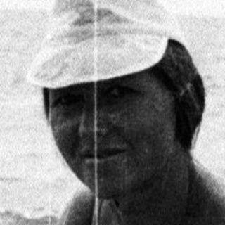 Woman in swimwear crouches in shallow water on beach.