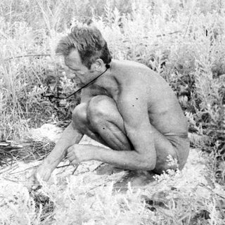 Man crouches amidst tall grass, appears to be working.