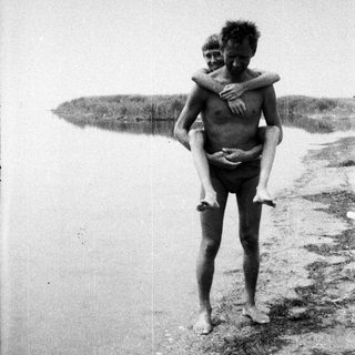 Man carries a child on his back near a body of water.