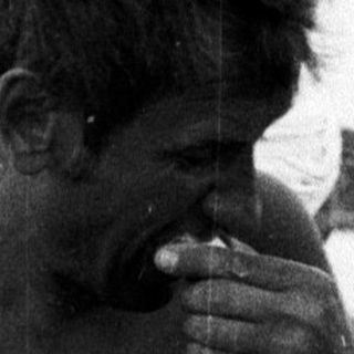 Man seated on beach, eating from a jar.