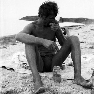 Man seated on beach, eating from a jar.