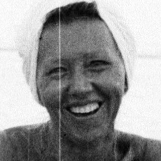 Woman eating on a beach, seated on a blanket.