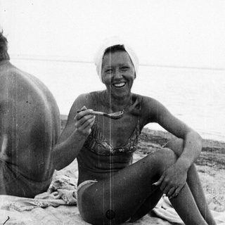 Woman eating on a beach, seated on a blanket.