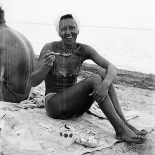 Woman eating on a beach, seated on a blanket.