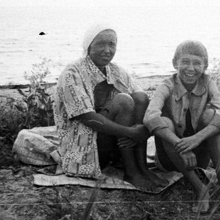 Two children sit on grassy bank near a body of water.