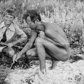Two young men sit in tall grass, seemingly relaxed.