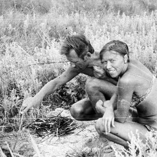 Two people kneeling in tall grass, outdoors.