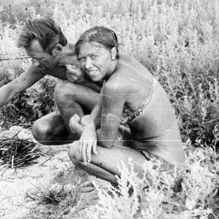 Two people kneeling in tall grass, outdoors.