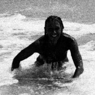Two figures in the water near a wave.