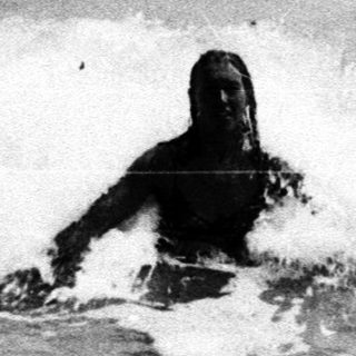 Black and white image of a person surfing a wave.