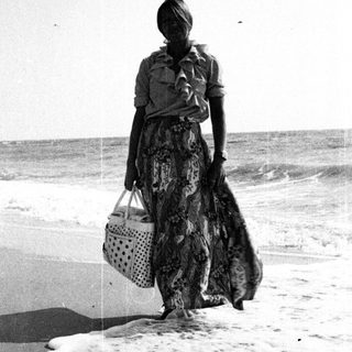 Woman walks along a beach holding a basket.