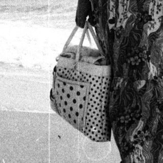 Woman walks along a beach holding a basket.
