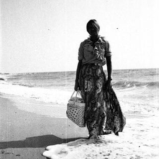 Woman walks along a beach holding a basket.