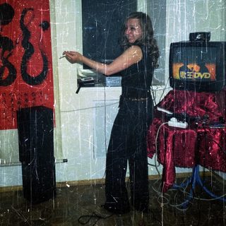 Woman stands near DVD player and red backdrop.