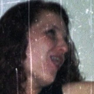 Woman in a dress with arms raised, blurred background.