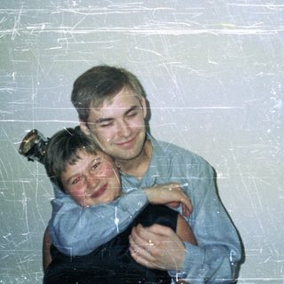 Man hugs child, woman stands nearby in a dark dress.