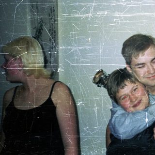 Man hugs child, woman stands nearby in a dark dress.