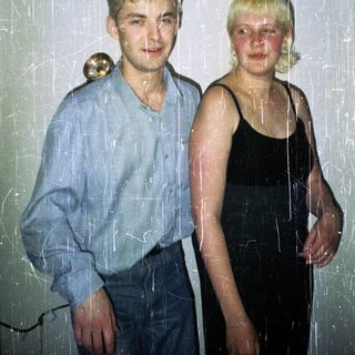 Here's a brief summary of the image: Young couple stands together, visibly aged photo with scratches.