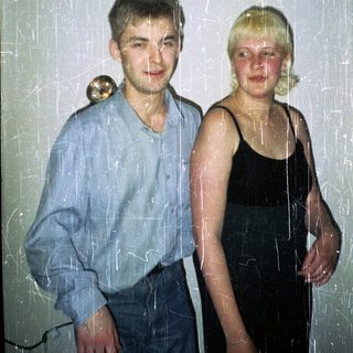 Here's a brief summary of the image: Young couple stands together, visibly aged photo with scratches.