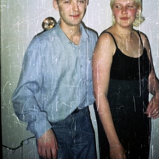 Here's a brief summary of the image: Young couple stands together, visibly aged photo with scratches.