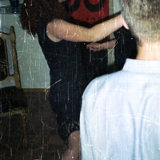Here's a brief summary of the image: Couple embracing indoors, with artwork visible in the background.