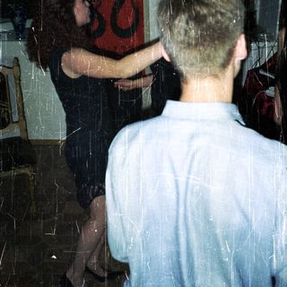 Here's a brief summary of the image: Couple embracing indoors, with artwork visible in the background.