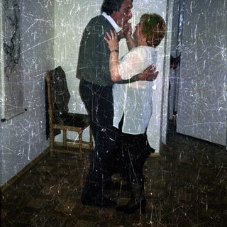 Man embraces a woman in a dimly lit room.