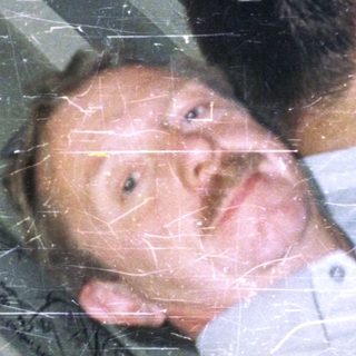 Man lies on floor near window, holding drinks.