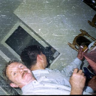 Man lies on floor near window, holding drinks.