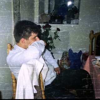 Young man seated, looking down, with roses in background.