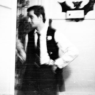 Man in suit holds papers, bat decoration visible.
