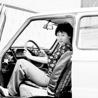 Woman seated in a vintage car, holding the steering wheel.