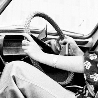 Woman seated in a vintage car, holding the steering wheel.