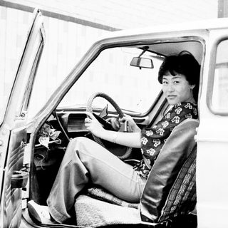 Woman seated in a vintage car, holding the steering wheel.